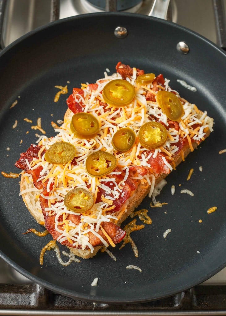 more shredded cheese and jalapenos have been laid out on top of a slice of bread in the non-stick pan