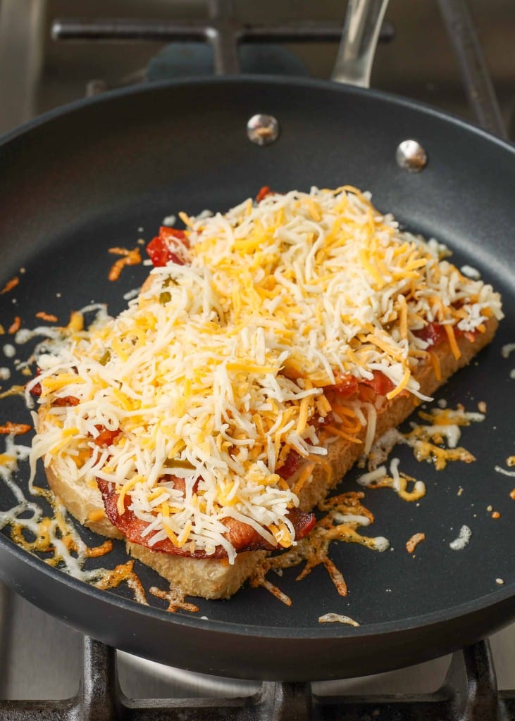 a final layer of shredded cheese has been added to the bottom half of the grilled cheese in a non-stick pan