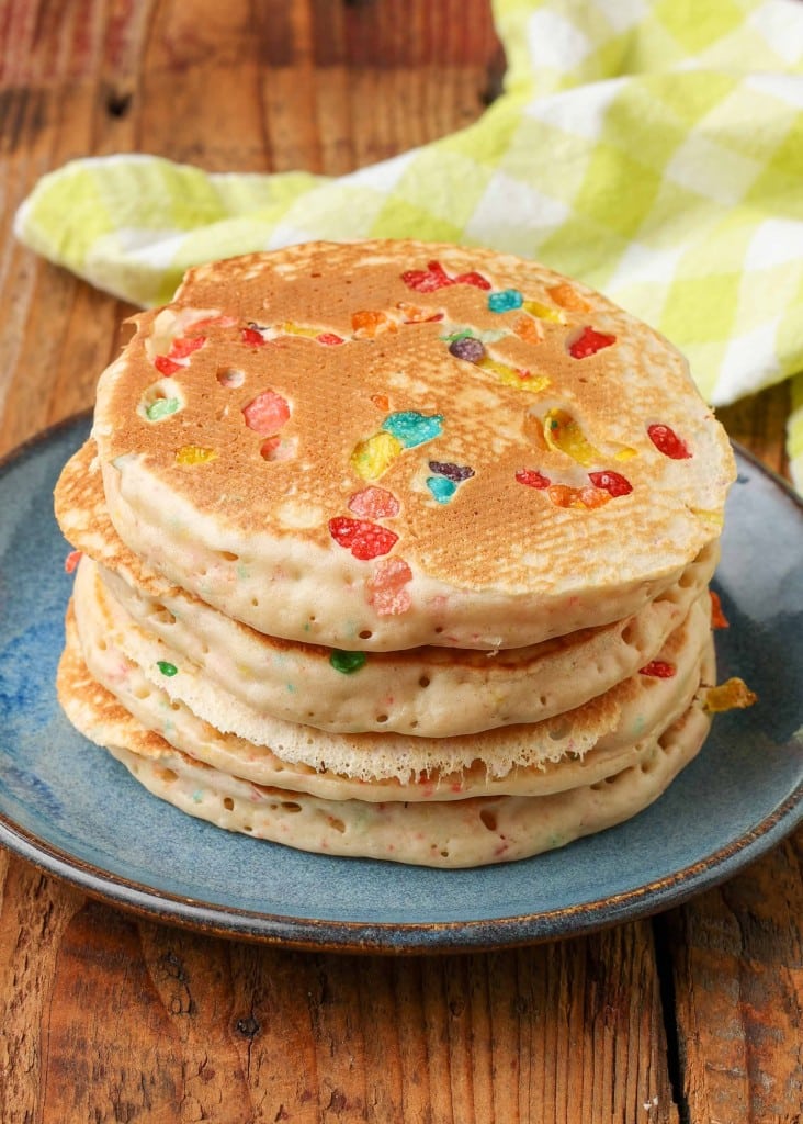 Fruity pebbles pancakes stacked on a blue plate with a striped yellow and white towel