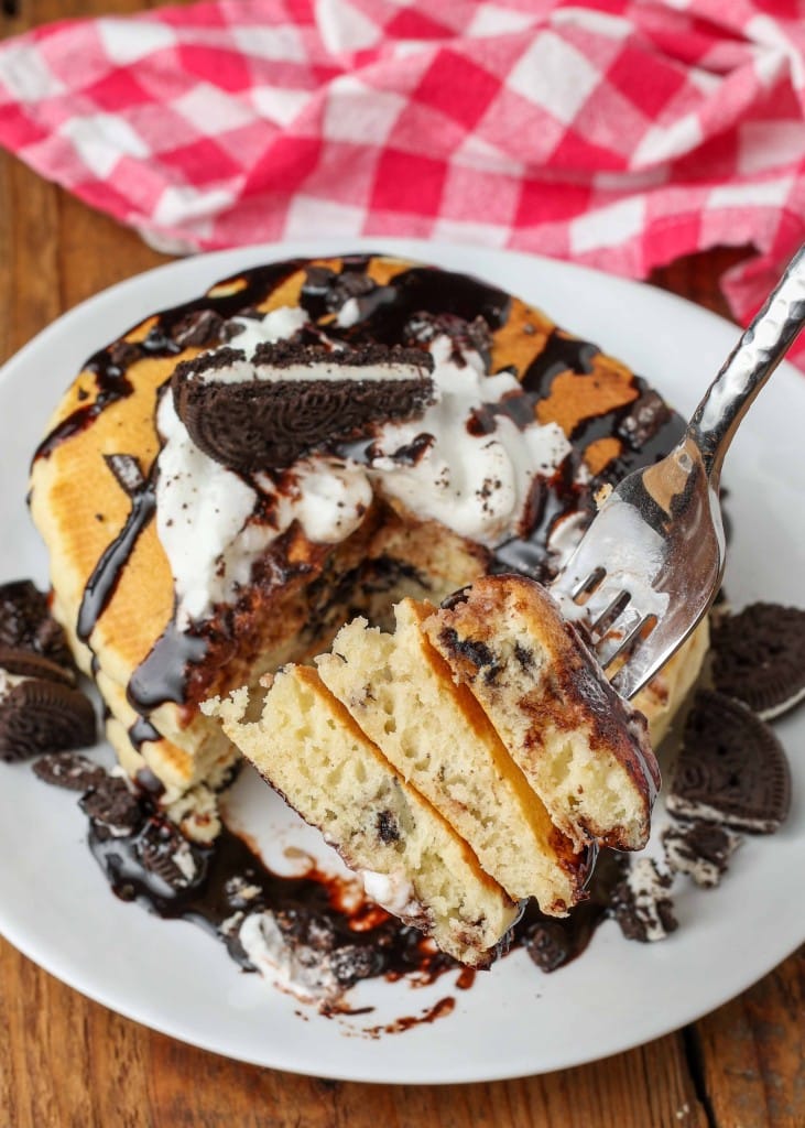 A wedge of three oreo pancakes has been sliced out of this stack and is on a fork, ready to eat!