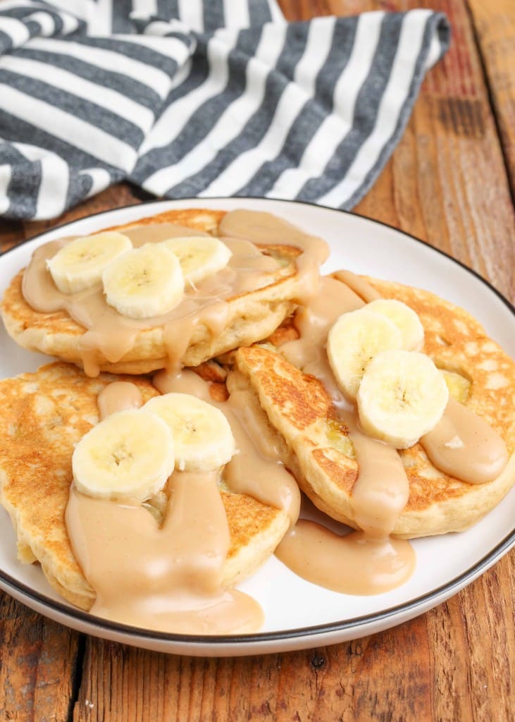 pancakes layered on plate with sliced bananas and peanut butter sauce