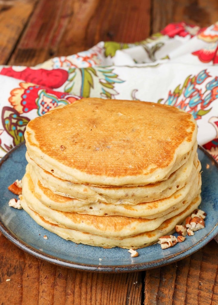 a stack of pecan pancakes on a blue plate with a colorful tea towel visible in the background.