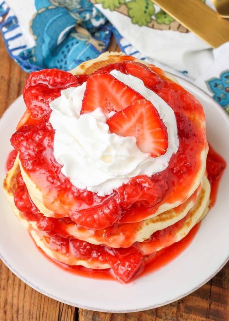 pancakes topped with strawberry sauce and whipped cream with berries on top