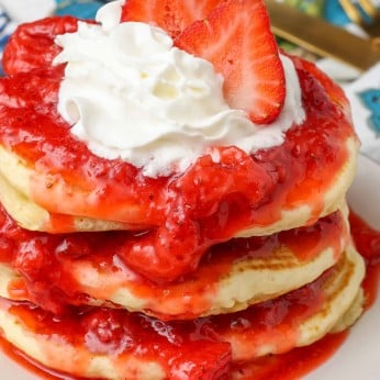 close up stack of pancakes with strawberry sauce and whipped cream