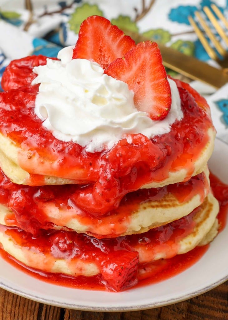 close up stack of pancakes with strawberry sauce and whipped cream