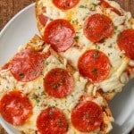 Two slices of Air Fryer French Bread Pizza on a white plate on a wooden tabletop.