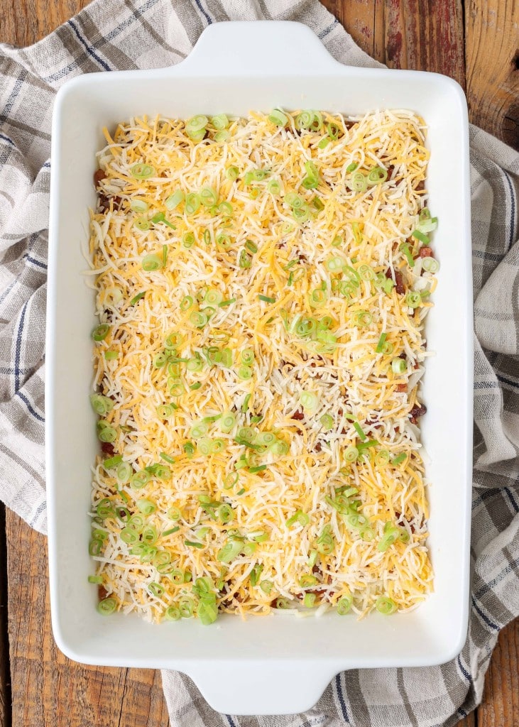 The hashbrowns, part of the shredded cheese, and the green onions have been layered in the baking dish.