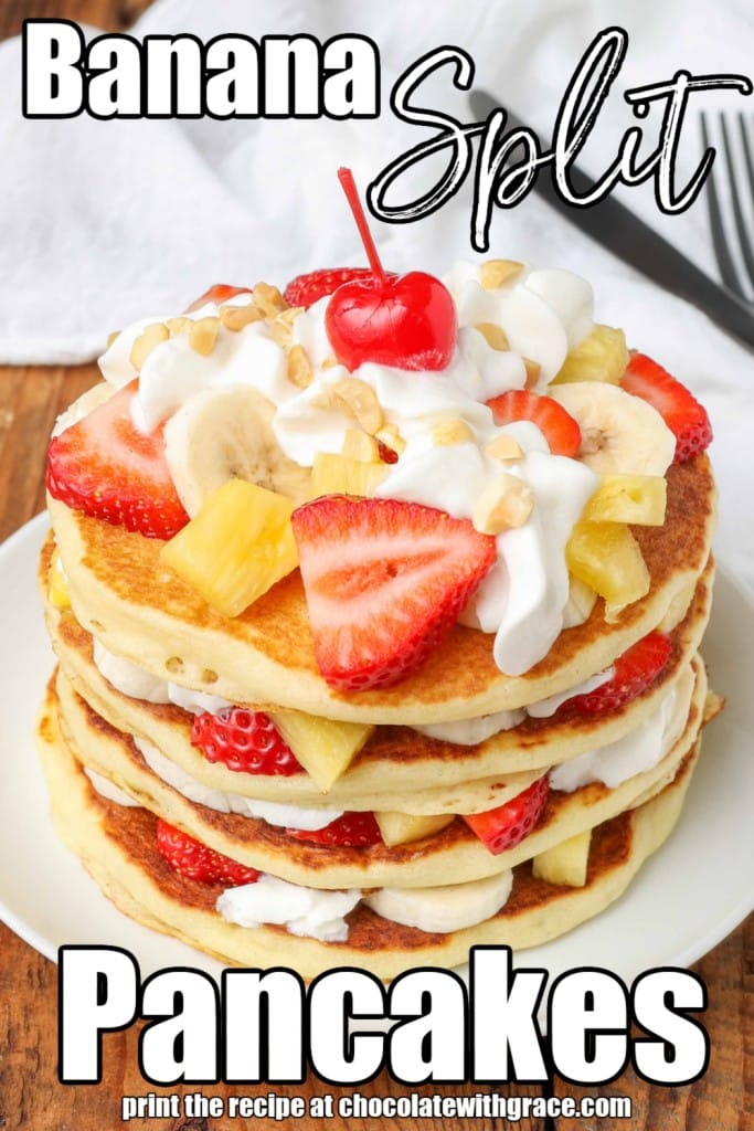 White lettering has been overlaid this image of pancakes that have been layered with whipped cream, bananas, strawberries, and pineapple tidbits. It reads, "Banana Split Pancakes".