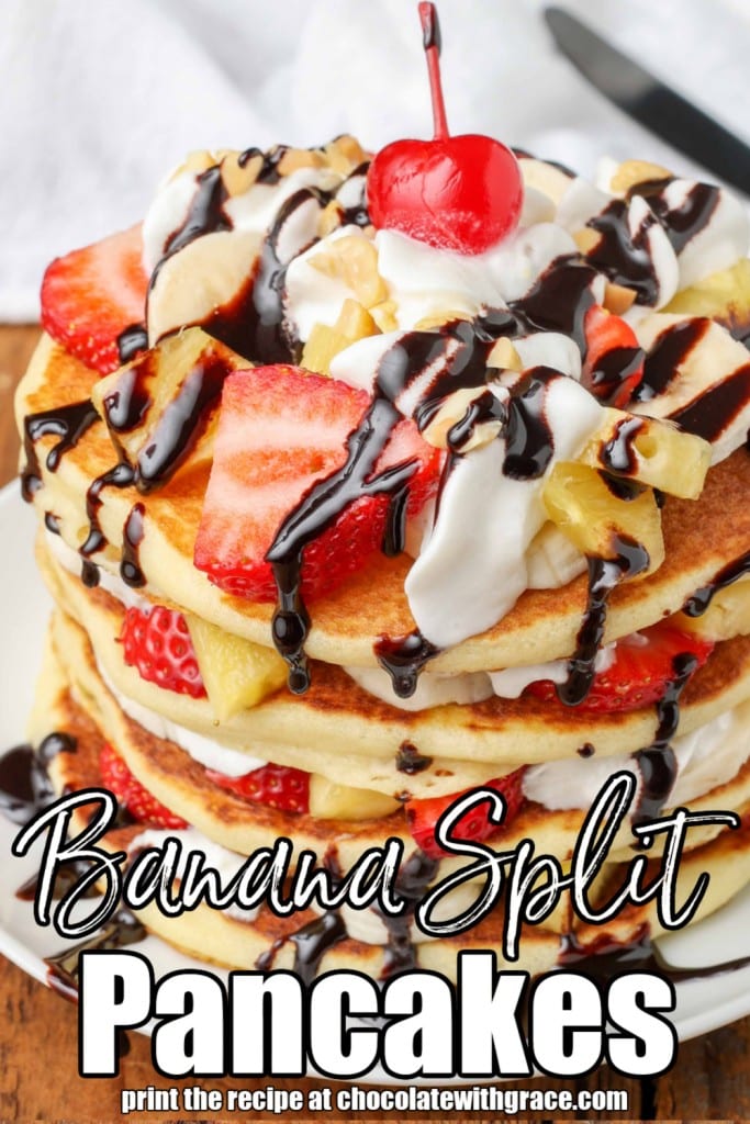 White lettering has been overlaid this image of a cherry that has been placed atop this stack of banana split pancakes with whipped cream and chocolate sauce. It reads, "Banana Split Pancakes".
