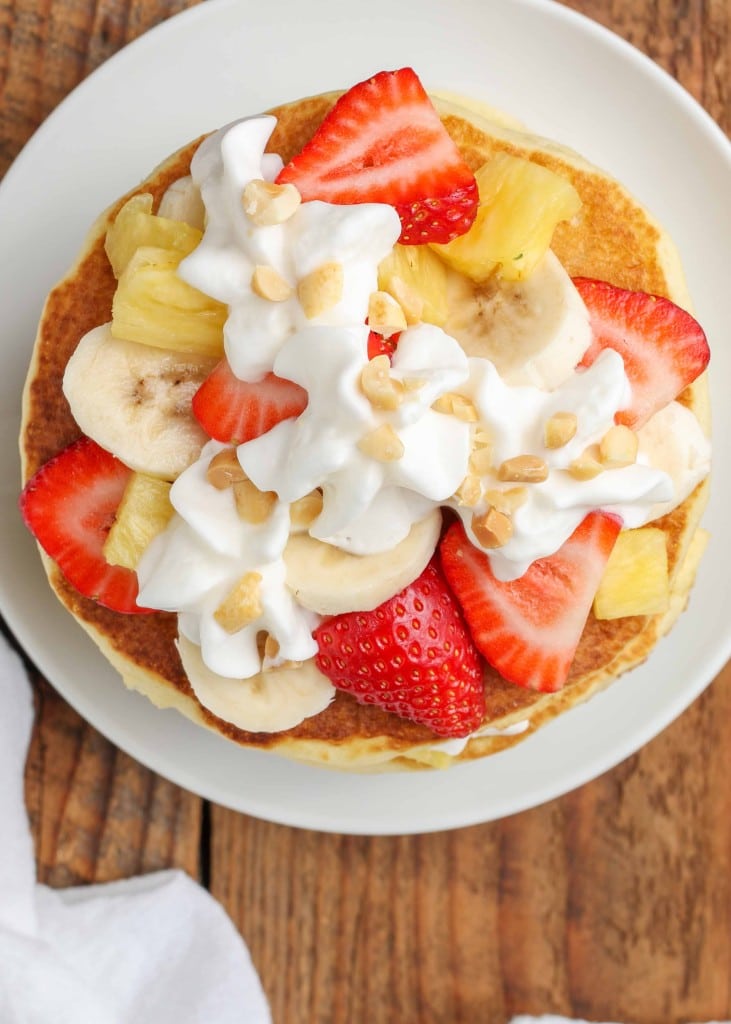 A top down shot of the stack of pancakes, topped with whipped cream and fresh fruit.