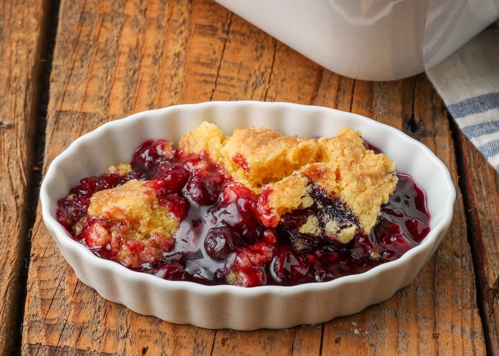 a horizontally aligned photo of a serving of dump cake with blueberries on a wooden tabletop.