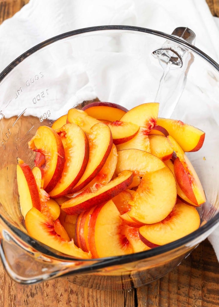 thinly sliced peaches are placed within a clear glass mixing bowl