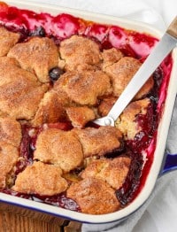a metal spoon has been inserted into the blueberry peach cobbler, lifting out a serving of the warm dessert.
