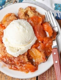 A top down photo of a plate of peach cobbler, topped with a scoop of vanilla ice cream.