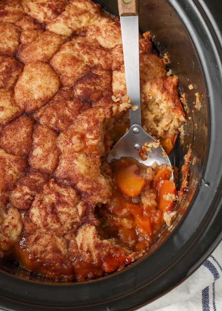 A serving has been scooped out of the crockpot peach cobbler, revealing the peaches under the topping.