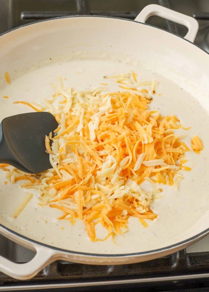 Shredded cheese has been added to the pan of seasoned cream. 