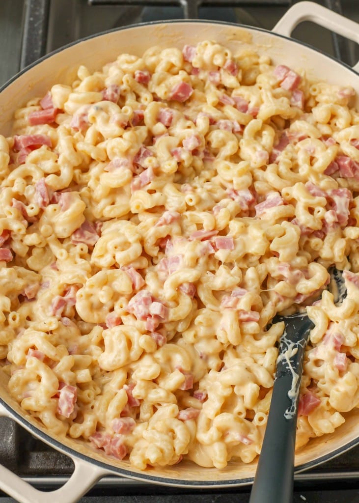 A vertically aligned photo of a white pan full of mac and cheese with ham, ready to be served.