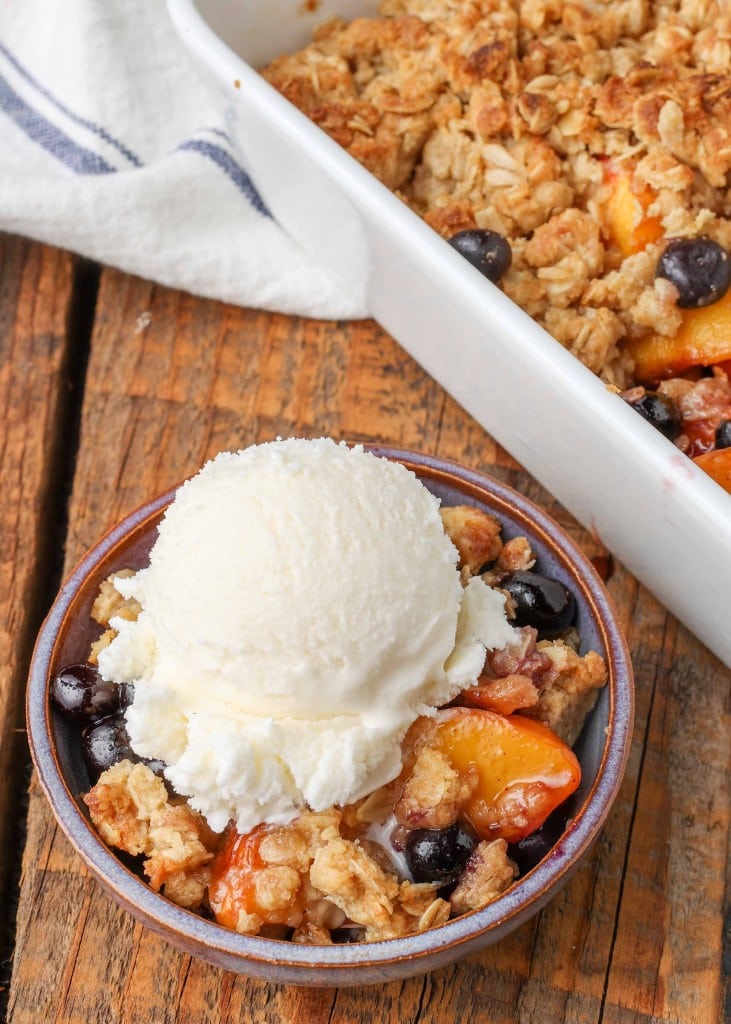 a close of shot of a serving of blueberry peach crisp in a small blue bowl with a scoop of vanilla ice cream on top.