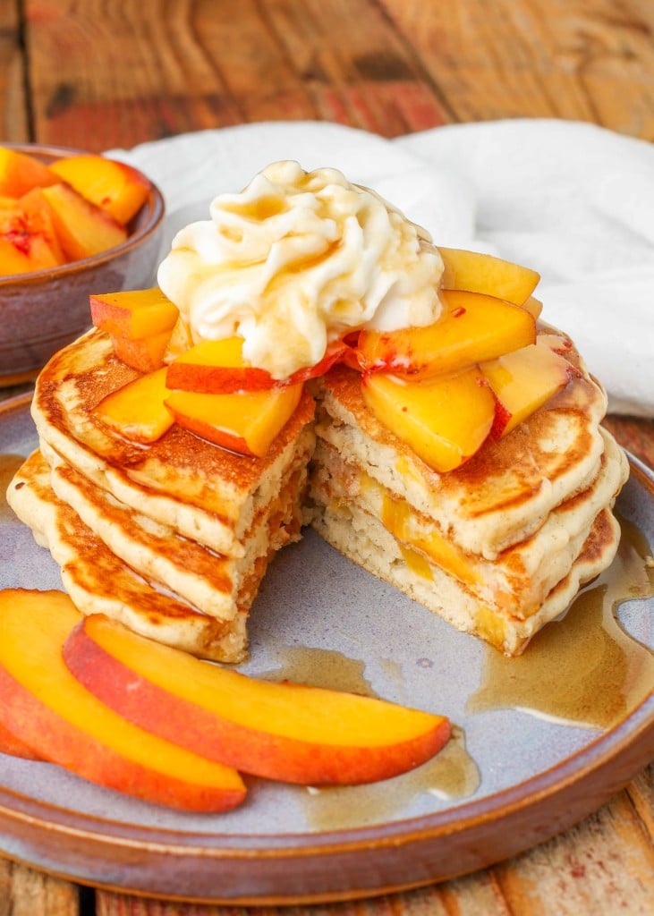 A wedge has been removed from a stack of peach pancakes on a light blue plate, revealing the tender peach pieces inside each pancake.