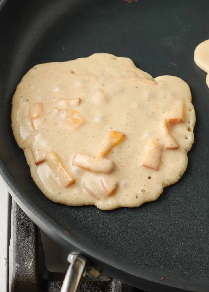 The chunks of peach are visible in the pancake batter where it has been scooped onto the griddle to cook.