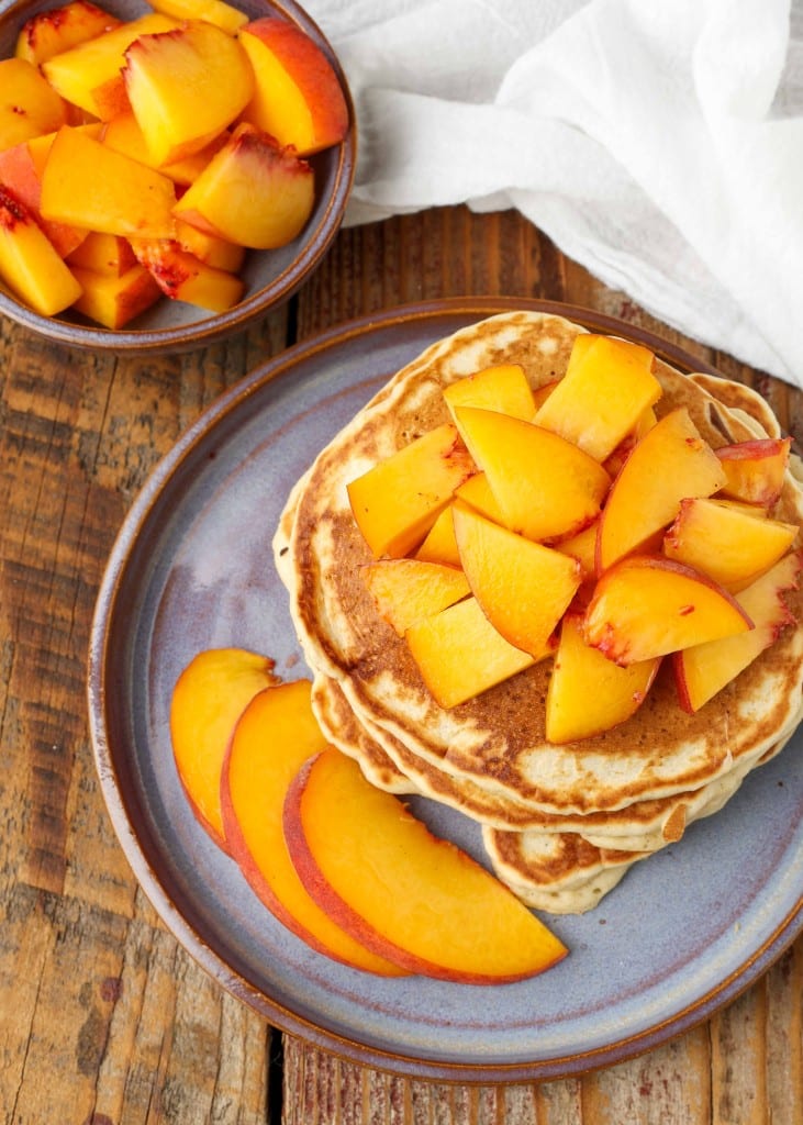 A top down photo of a stack of peach pancakes with peaches sprinkled on top to create a topping.