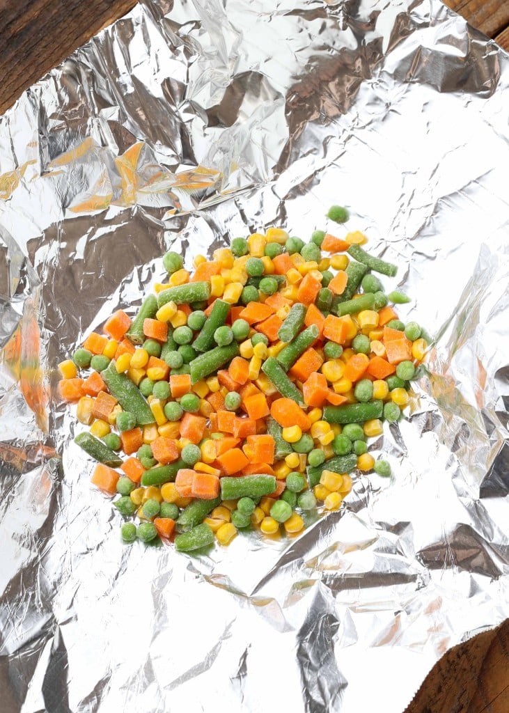 Overhead shot of frozen peas, corn, green beans, and diced carrots in a foil sheet