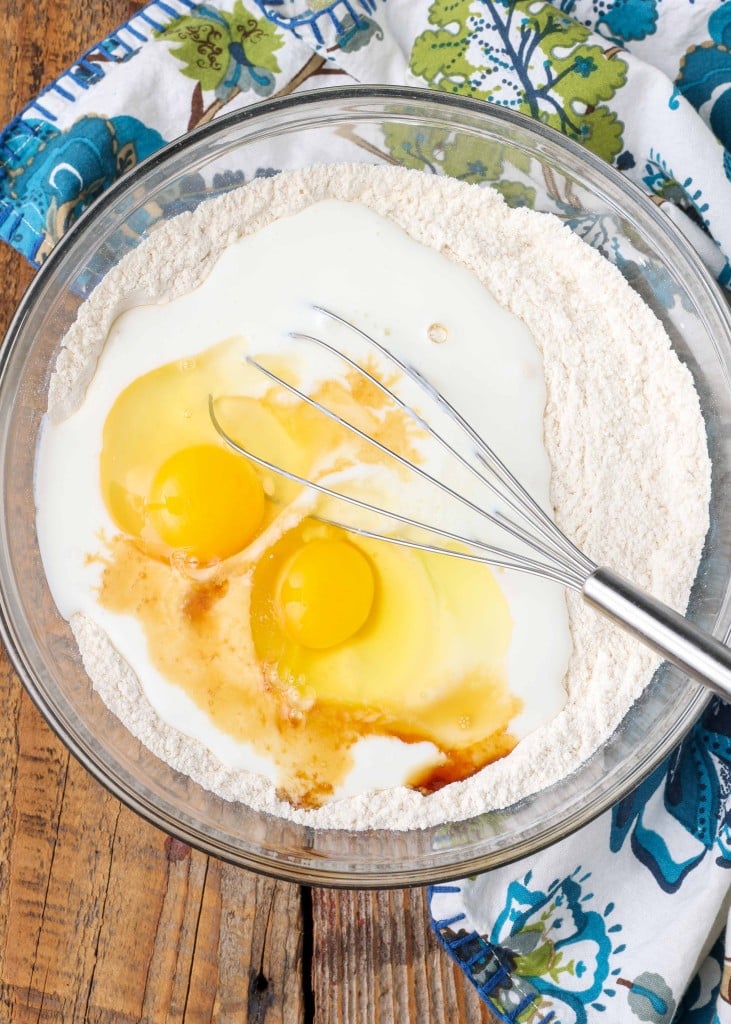 Overhead vertical shot of flour, buttermilk, and eggs in a glass bowl with a silver whisk