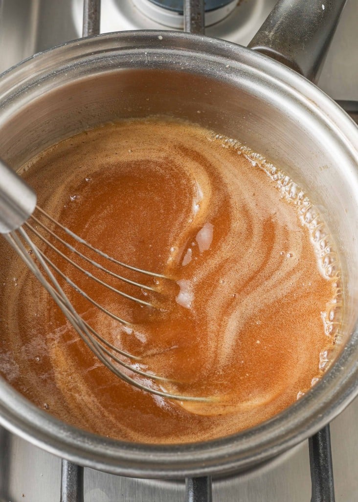Overhead shot of butter, brown sugar, and buttermilk in saucepan being stirred by a silver whisk