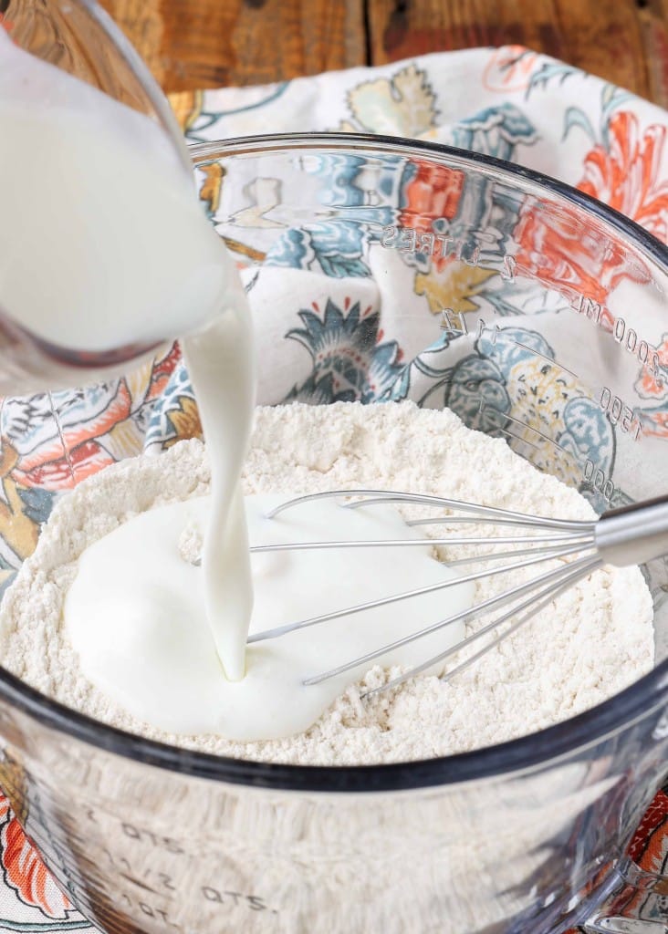 Vertical shot of flour and milk in a glass dish with a silver whisk