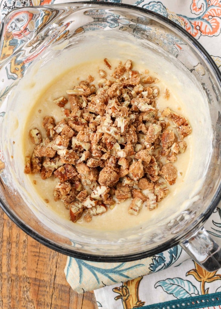 Overhead shot of cake batter and chopped pecans in a glass dish with a floral pattern hand towel