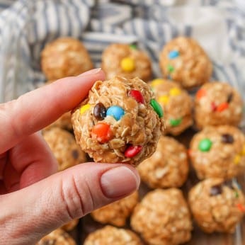 a close up shot of a single peanut butter oatmeal ball, held by thumb and finger, with more candies visible in the background