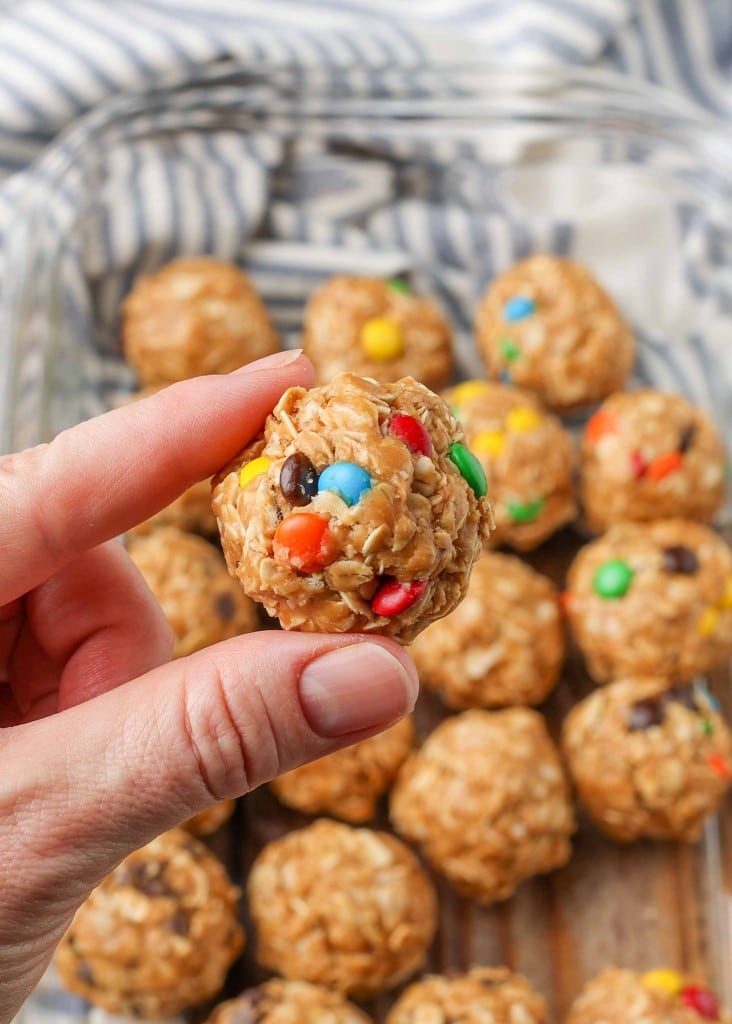 a close up shot of a single peanut butter oatmeal ball, held by thumb and finger, with more candies visible in the background