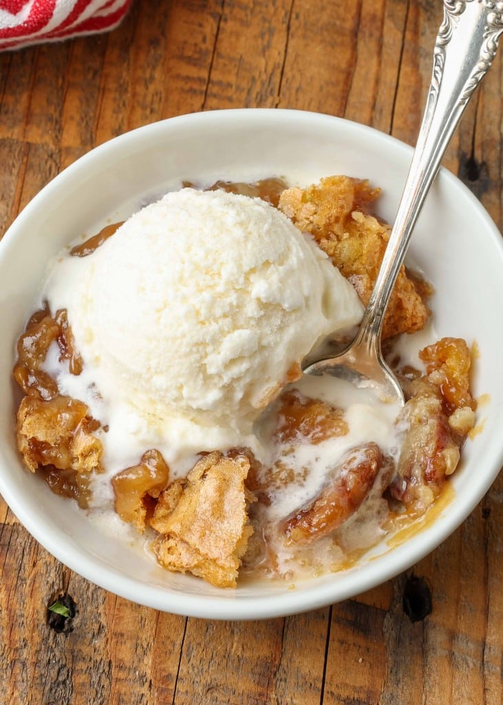 scoop ice cream over a dish of cobbler with pecans on wooden table