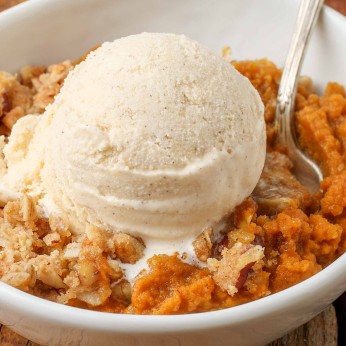 A close up shot of a scoop of vanilla ice cream slowly melting into a serving of pumpkin crisp.