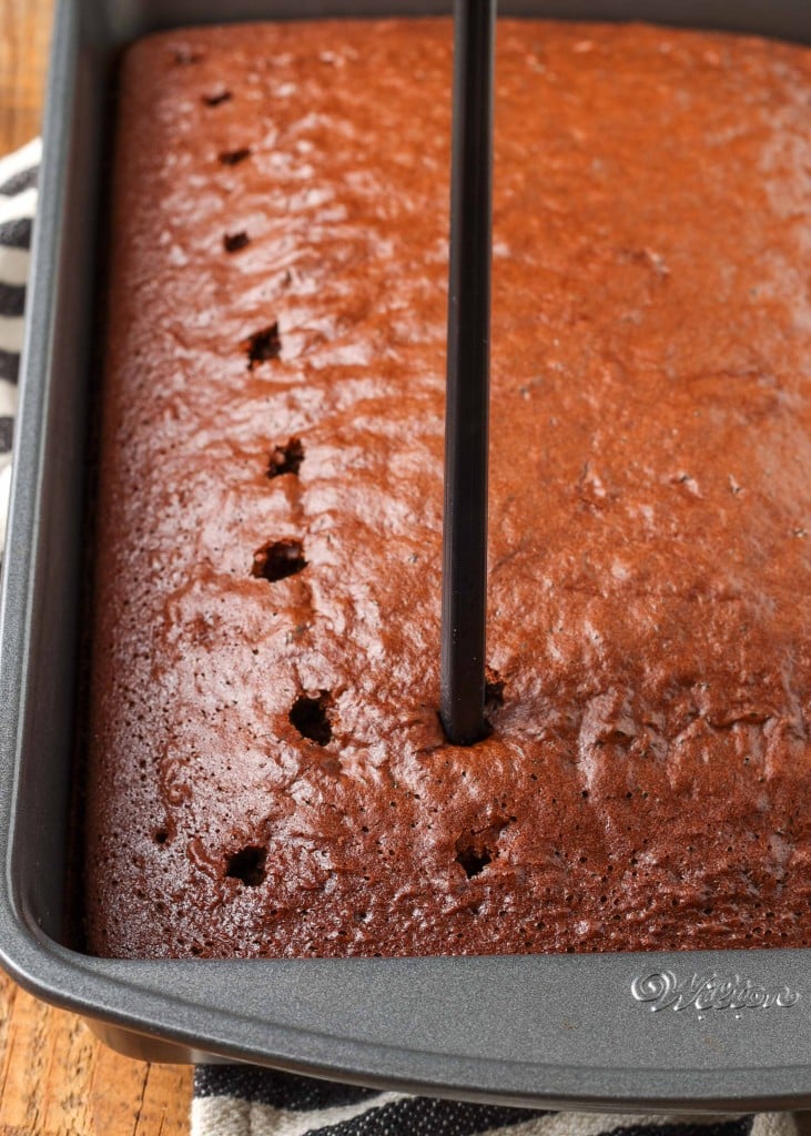 action shot of poking holes into the baked chocolate cake in the metal pan