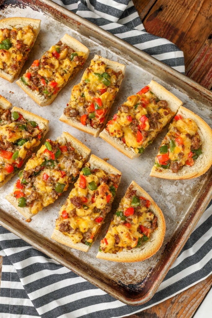 Overhead shot of sliced French bread with sausage, bell peppers, cheese, eggs, and onions