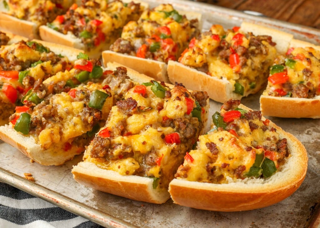 Close-up on sliced French bread with sausage, bell peppers, cheese, eggs, and onions