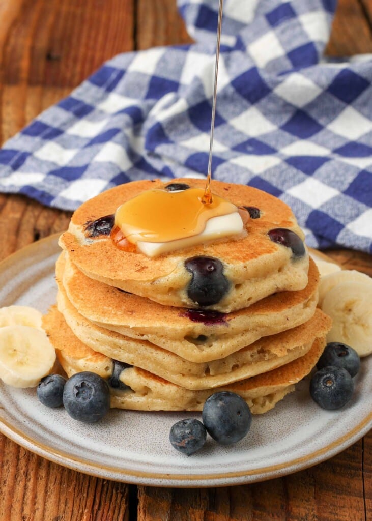 Drizzling syrup over berry pancakes with banana slices and butter