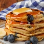 Vertical shot of berry pancakes topped with a pat of butter, maple syrup, and banana slices