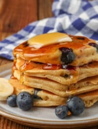Vertical shot of berry pancakes topped with a pat of butter, maple syrup, and banana slices