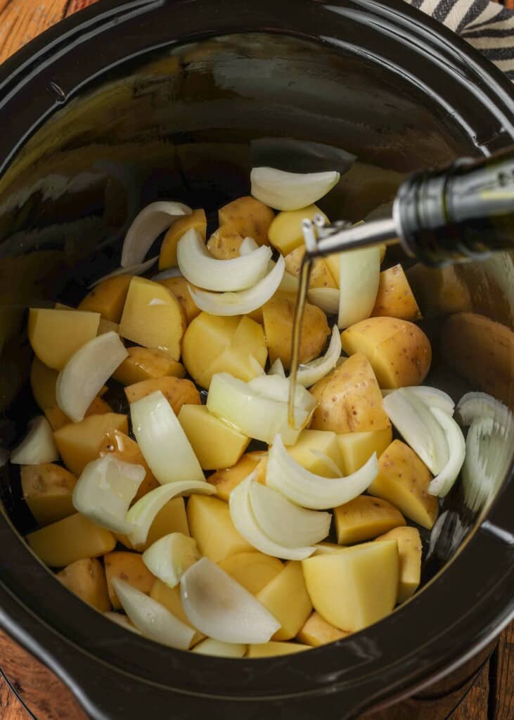 Drizzling oil over potatoes and onions in slow cooker