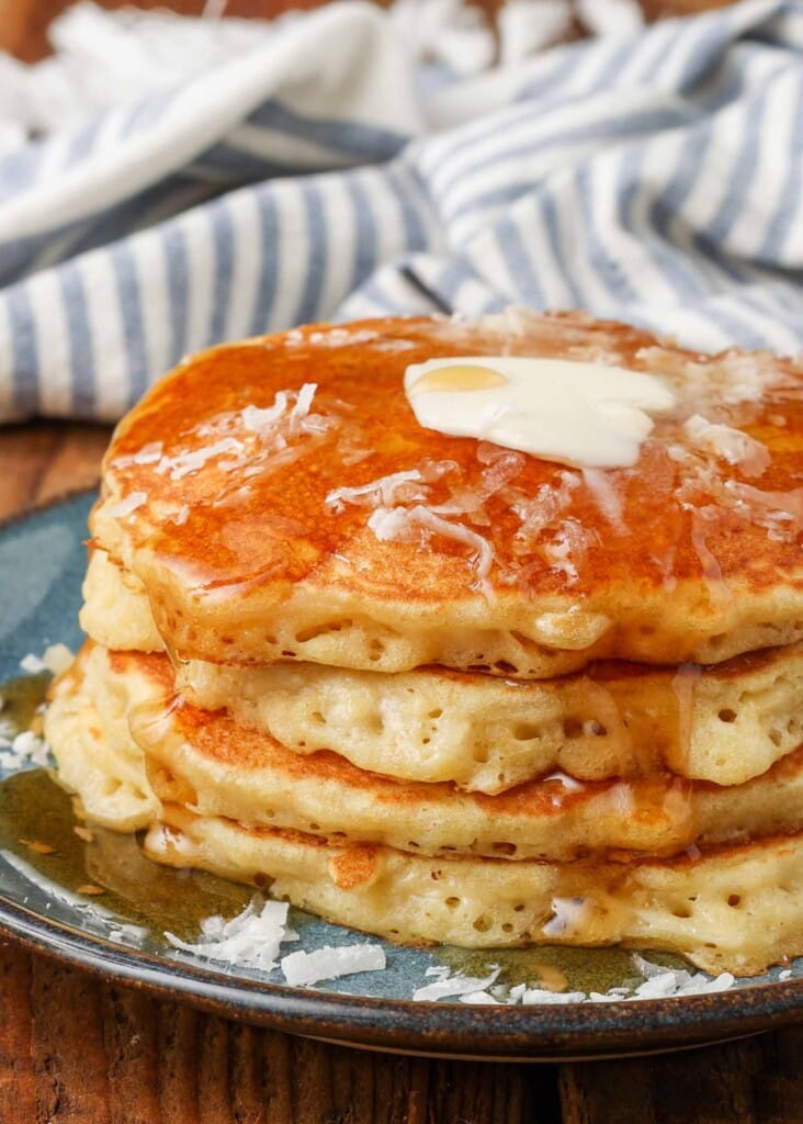 close up photo of pancakes with pineapple and coconut stacked on plate