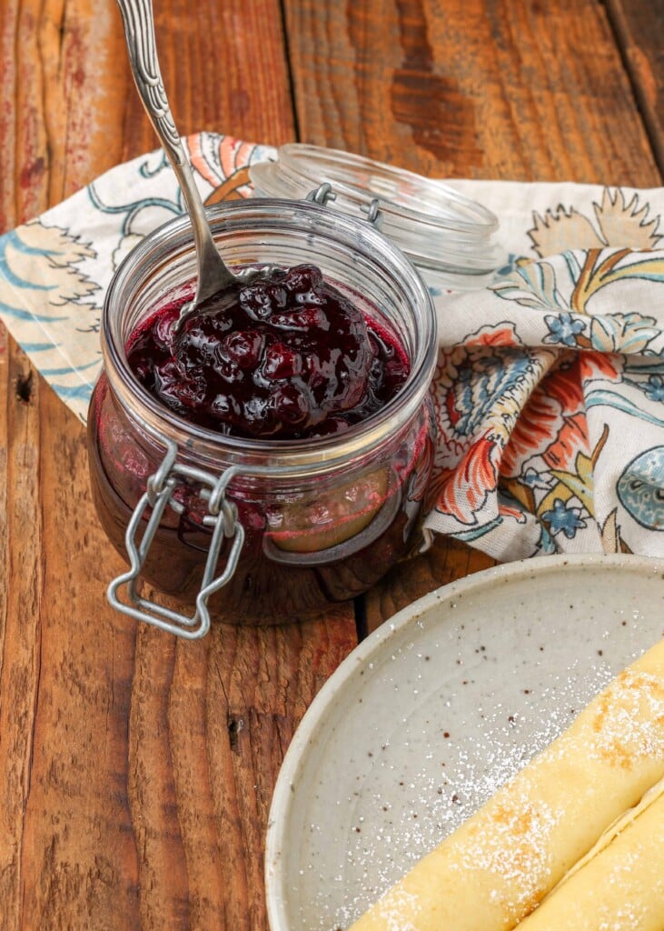 Blueberry Compote in jar next to a plate of crepes