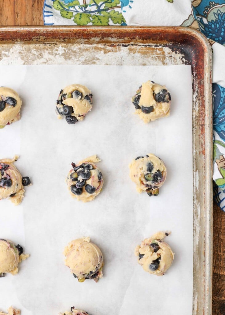 Balls of cookie dough with blueberries spread across baking tray