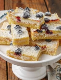 stacked lemon blueberry bars on white stand on wooden table