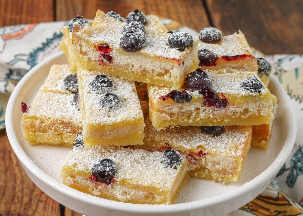 sliced lemon bars with blueberries in them stacked on a plate