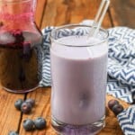 A vertical shot of the blueberry milk in a glass with a glass straw.