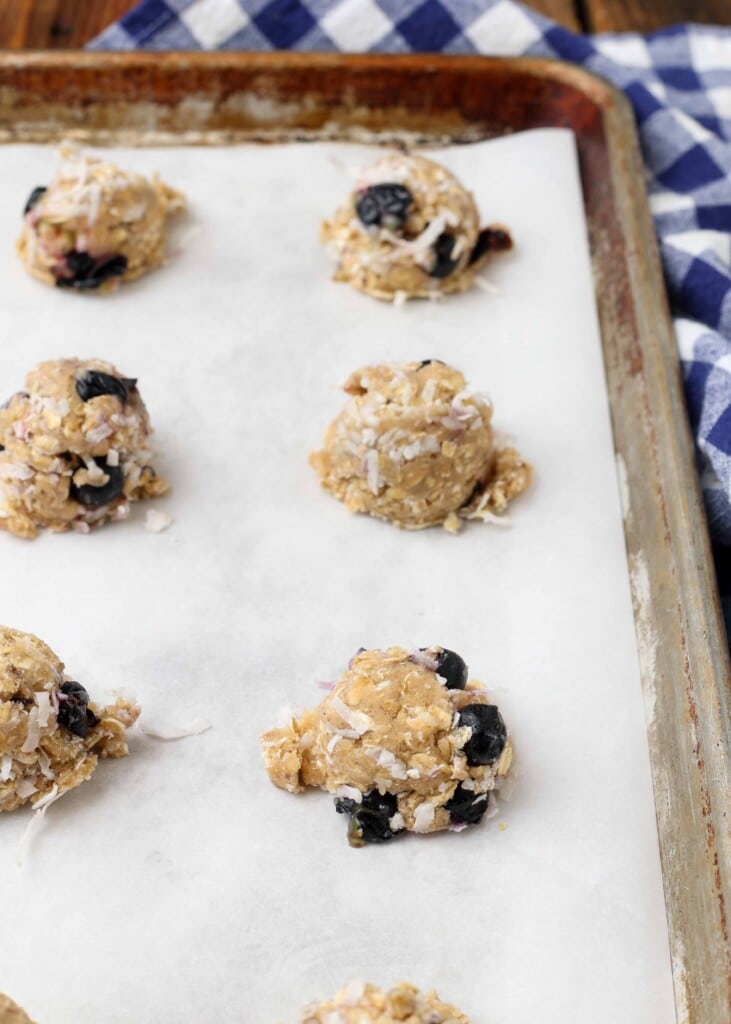 Balls of blueberry oatmeal cookie dough on a parchment paper-lined baking sheet.