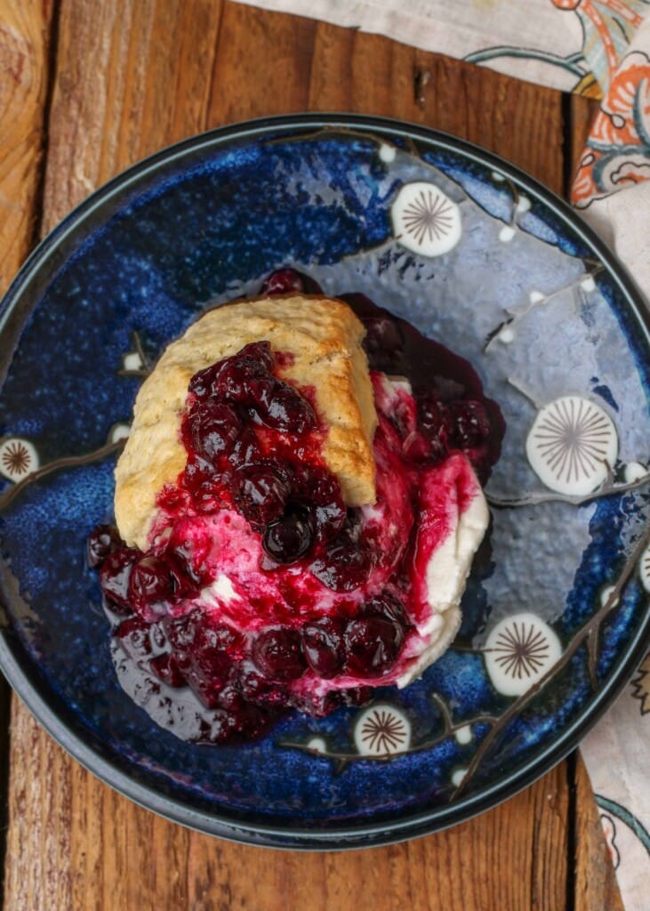 an overhead shot of blueberry shortcake with vanilla ice cream and blueberry compote on a dark blue ceramic plate.