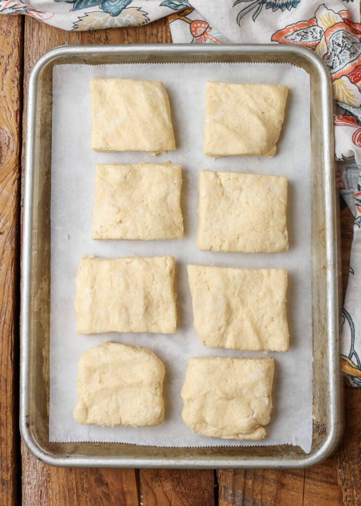 The shortcakes have been sliced and are laid in two rows on a parchment paper - lined baking sheet.